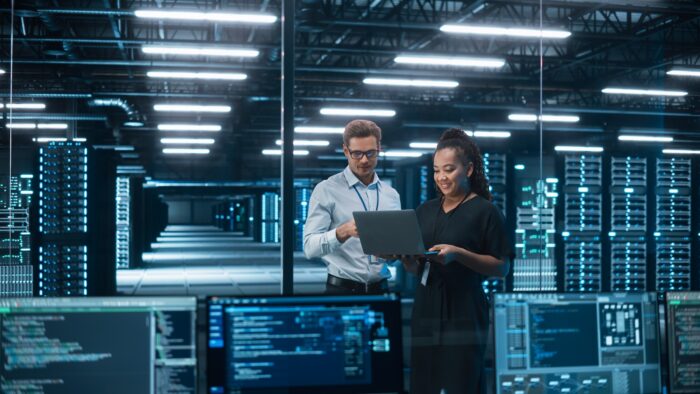 Two people in a server room looking at a laptop