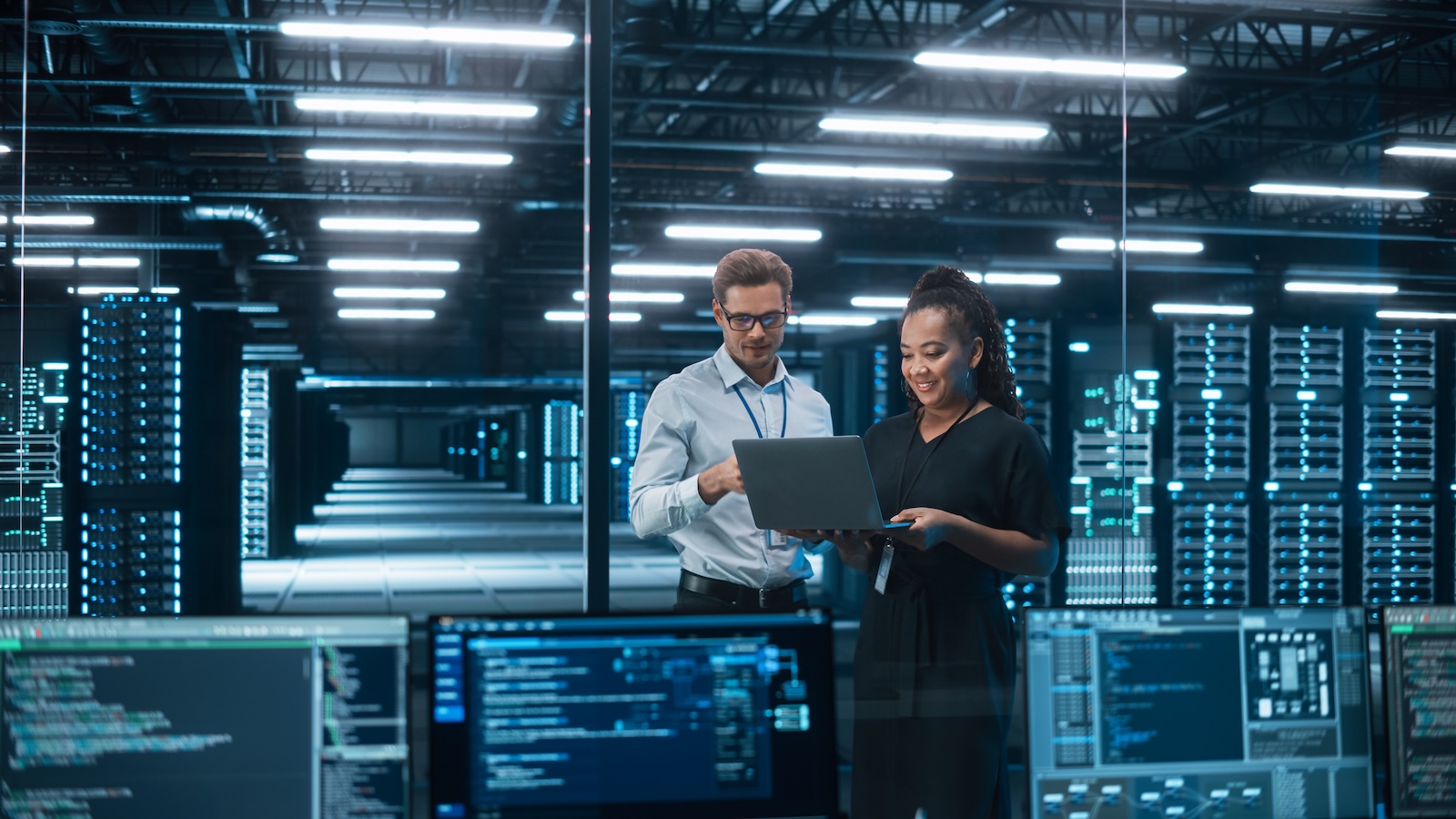 Two people in a server room looking at a laptop