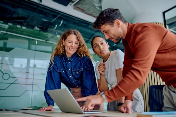 Diverse business team collaborating and discussing project strategy, pointing at laptop screen in a modern office